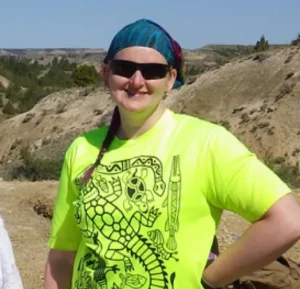 FMSM supporter Becky B. standing outside in a glue bandana, black sunglasses and a neon yellow shirt with an illustration of reptiles on it.