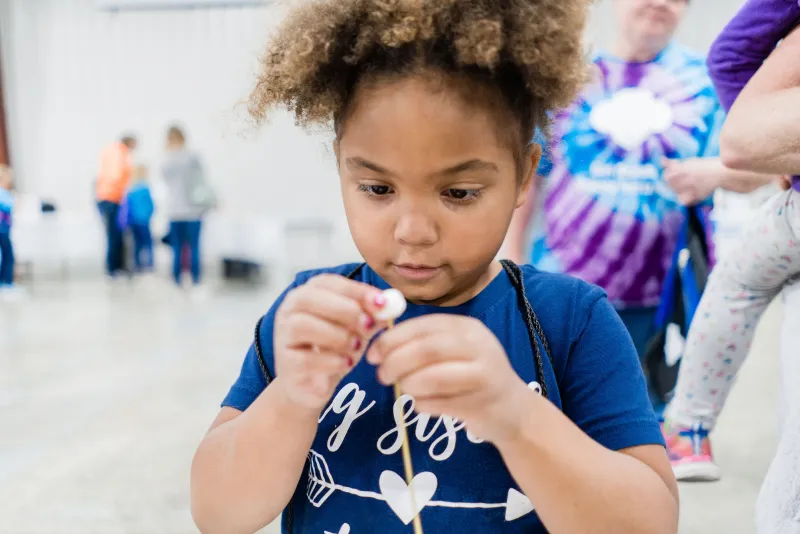Image of a child interacting with a spaghetti noodle and marshmallow activity. Participant can use the marshmallows to connect the noodles and build structures.